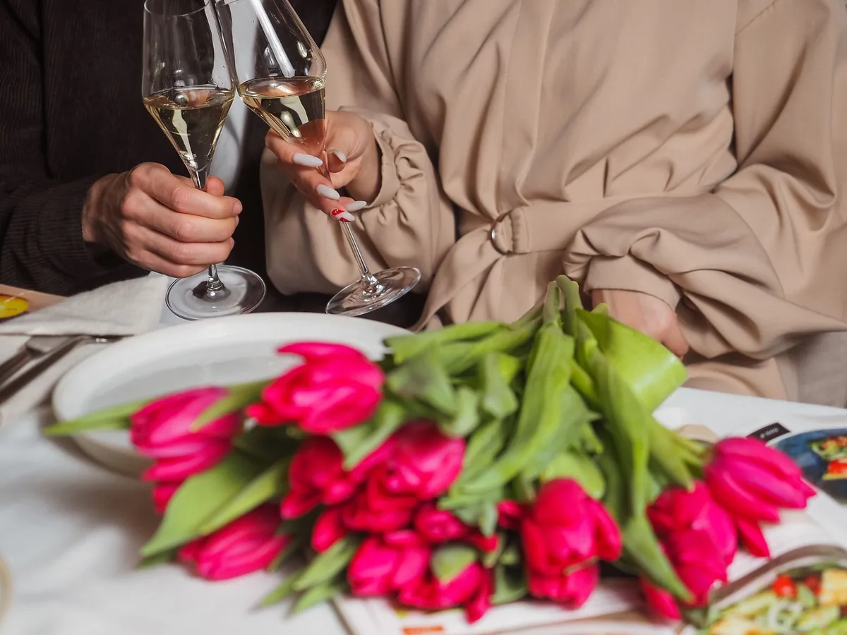 pár si přiťukává skleničkami vedle kytice tulipánů